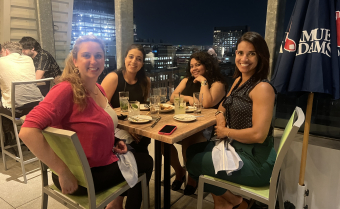 Photo of Four Women Sitting at a Table in Front of Large Window at Night